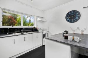 a kitchen with white cabinets and a clock on the wall at Archie's Beach Bach - Orewa Accommodation in Orewa