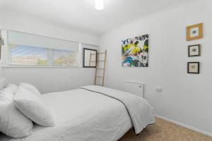 a white bedroom with a bed and a window at Calapso Cottage - Waikanae Beach Holiday Home in Waikanae