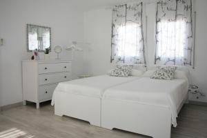 a white bedroom with a white bed and two windows at Apartamento Cambrils Duplex in Cambrils