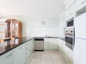 a white kitchen with white cabinets and black counter tops at Castillo Del Mar 10 in Tuncurry