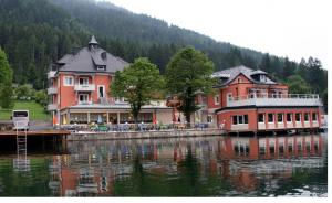 un gran edificio en el agua junto a un lago en Strandhotel Burgstaller, en Feld am See