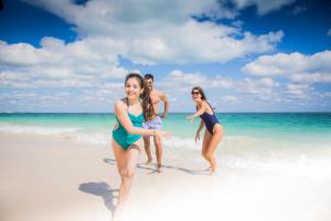 
two girls are walking on the beach with their surfboards at Majestic Elegance Costa Mujeres - All Inclusive in Cancún
