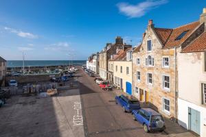 a street with buildings and cars parked next to the ocean at The Old Chandlery in Pittenweem