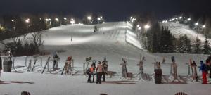 un grupo de personas de pie en una pista de esquí por la noche en Studio-hôtel Villegiature Saint-Sauveur, en Piedmont