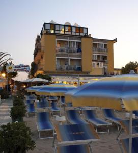 eine Reihe von Stühlen und Sonnenschirmen vor einem Gebäude in der Unterkunft Hotel Estate in Rimini