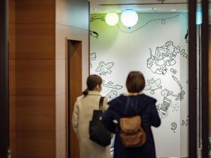two women looking at a wall with drawings on it at KOKO HOTEL Ikebukuro East in Tokyo