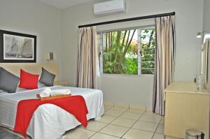 a bedroom with a bed with a red blanket and a window at Sunrise Beach Resort in Amanzimtoti