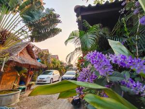eine Straße mit geparkten Autos und lila Blumen in der Unterkunft Bua Patumma Resort in Mae Sai