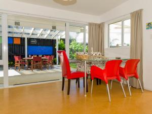a dining room with red chairs and a table at Gone Coastal - Whangamata Holiday House in Whangamata