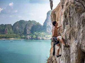 a man rock climbing on a cliff next to a lake at K-Bunk Hostel in Ao Nang Beach