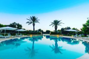 a large swimming pool with palm trees and umbrellas at Masseria Valente in Ostuni