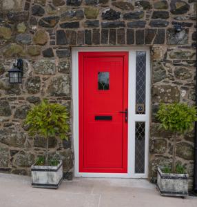 a red door on a stone wall with two potted plants at The Barn at BallyCairn in Larne
