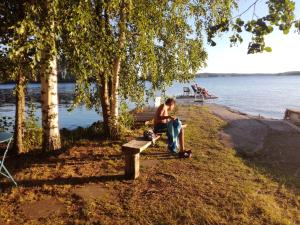a man sitting on a bench next to the water at Nestorinranta Resort in Lintusalo