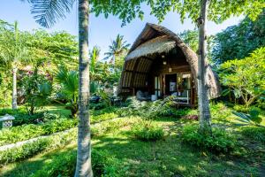 una casa con techo de paja en un jardín con palmeras en Kelapa Cottage, en Amed