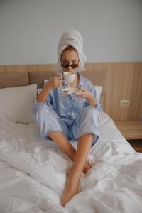 uma mulher sentada numa cama a beber uma chávena de café em Hotel panorama svaneti em Mestia