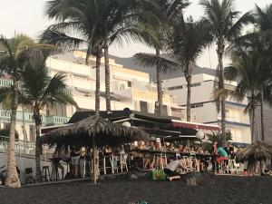 a group of people sitting at a beach with palm trees at Pauval Sunset in Puerto Naos