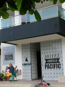 Hotel OBEGA PACIFIC في نوكوي: امرأة تجلس على مقعد أمام فندق المحيط الهادئ