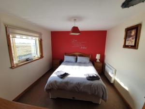 a bedroom with a bed with a red wall at Taigh nam Piobaireach in Balivanich