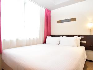 a hotel room with a white bedspread and white pillows at ibis Styles Kyoto Station in Kyoto