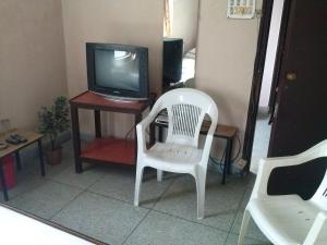 a living room with a tv and a white chair at Capital Guest House in Kolkata