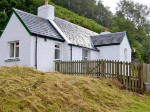 ein kleines weißes Haus mit einem Holzzaun in der Unterkunft Roddy's Cottage in Glenelg