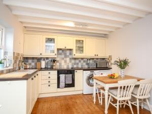 cocina con armarios blancos y mesa de madera en The Granary - Rhoscolyn, en Holyhead