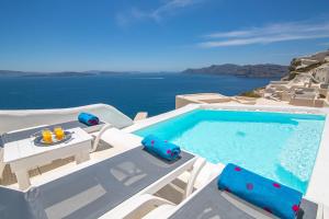 een zwembad met stoelen en een tafel en de oceaan bij Alexander's Suites in Oia