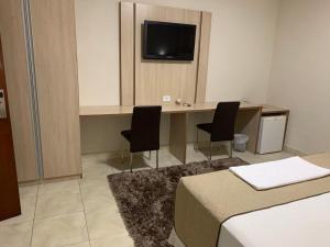 a room with a desk with two chairs and a television at Hotel Arlen in Pouso Alegre