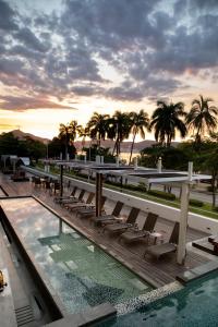 a deck with chairs and a pool with palm trees at Ramada by Wyndham Acapulco Hotel & Suites in Acapulco