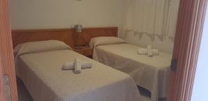 2 bedden in een kleine kamer met witte lakens bij Apartamentos Can Miguel in Cala San Vicente