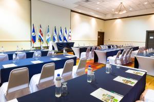 Holiday Inn San Salvador, an IHG Hotel في سان سلفادور: غرفة بها طاولات زرقاء وكراسي بيضاء وأعلام