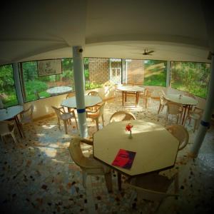 a dining room with tables and chairs and windows at New Creation Guest House in Auroville