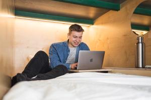 un uomo seduto su un letto usando un computer portatile di Green Marmot Capsule Hotel Zürich a Zurigo