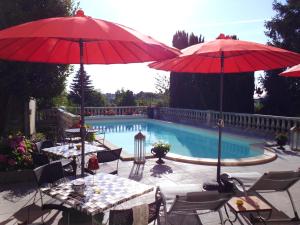 two tables with red umbrellas next to a swimming pool at Le PETIT CHATEAU - Tiffauges proche Puy duFou in Tiffauges