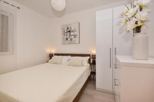 a white bedroom with a bed and a vase of flowers at Apartman Luka in Igrane