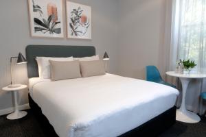 um quarto com uma cama branca com duas mesas e uma janela em The Alison Randwick em Sydney