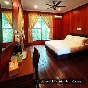 a bedroom with a bed and a desk and windows at Kinabatangan Wildlife Lodge in Sandakan