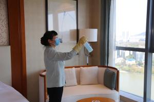uma mulher num quarto de hotel usando uma máscara e limpando uma janela em Yiwu Shangcheng Hotel em Yiwu