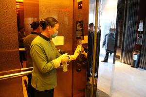 uma mulher com uma máscara e luvas a abrir uma porta em Yiwu Shangcheng Hotel em Yiwu