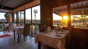 uma sala de jantar com mesas, cadeiras e janelas em De Zeekoe Guest Farm em Oudtshoorn