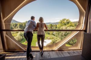 un homme et une femme debout devant une grande fenêtre dans l'établissement Seepark Wörthersee Resort, à Klagenfurt am Wörthersee