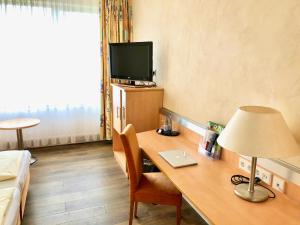 a room with a desk with a lamp and a tv at Hotel Central in Frankenthal