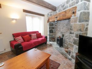 a living room with a red couch and a stone fireplace at 2 Hwyrfryn Stables in Penmaen-mawr