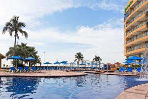 una piscina en un complejo con sillas y sombrillas azules en Holiday Inn Veracruz-Boca Del Rio, an IHG Hotel, en Veracruz