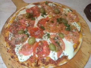 una pizza con tomates y aceitunas en una tabla de cortar de madera en Casa La Serena en Los Reartes