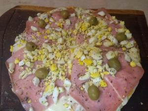 una pizza con jamón y aceitunas en una tabla de cortar en Casa La Serena en Los Reartes