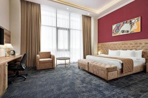 シムケントにあるRamada by Wyndham Shymkentのベッド、デスク、椅子が備わるホテルルームです。