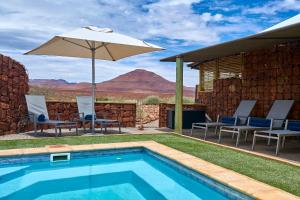 einen Pool mit einem Sonnenschirm, Stühlen und einem Tisch in der Unterkunft Etendeka Mountain Camp in Damaraland