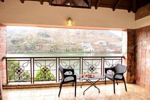 einen Balkon mit 2 Stühlen und einem großen Fenster in der Unterkunft Neelesh Inn- A Luxury Lake View Hotel- 20 kms from Nainital in Bhīm Tāl
