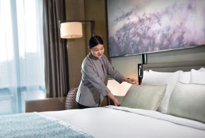 kobieta stojąca obok łóżka w pokoju hotelowym w obiekcie Crowne Plaza Shanghai Pujiang, an IHG Hotel w Szanghaju